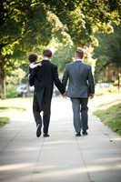 Two grooms hold hands while they stroll down the side walk with their young son