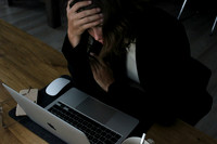 A woman holds her head as she struggles to get her work done.