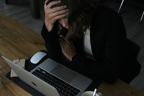 A woman holds her head as she struggles to get her work done.
