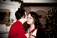 Two Brides wearing Black and Red kiss in front of a Christmas tree on their wedding day