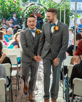 Two Grooms wearing gray tuxes walks up the aisle after getting married
