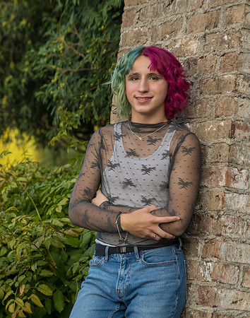 A boy with Magenta and teal hair stands against a Brick wall in his Senior Portraits