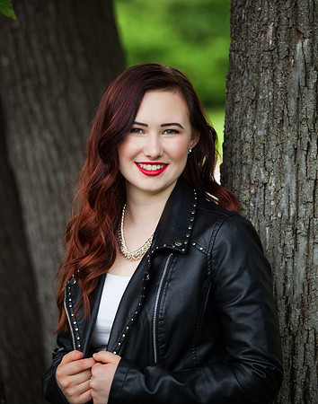 An Auburn haired girl wearing a black leather coat poses for her Senior Portraits.