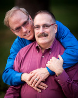 Two men dressed in button down shirts pose for their engagement session at the Harriet Rose Garden