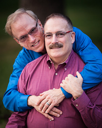 Two men dressed in button down shirts pose for their engagement session at the Harriet Rose Garden