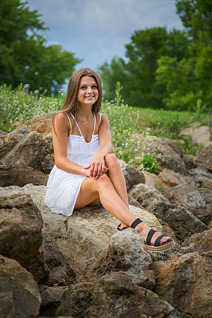 A High School Senior girl wearing a white dress poses on rocks in a wildflower field